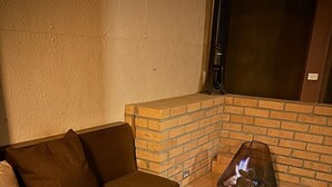 Ein gemütlicher Außenbereich mit einem Kamin aus Ziegelsteinen, einer Couch und zwei kleinen Tischen mit Weingläsern.