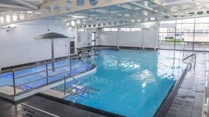 An indoor swimming pool with a clear water surface, a diving platform, and a poolside area with a safety railing. - Lovely 3-bed Caravan in Towyn (Abergele)