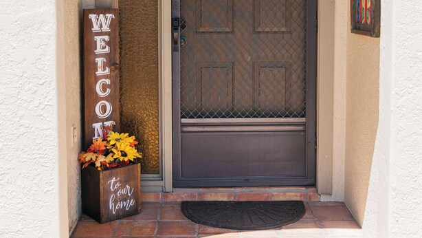 A front door with a 'WELCOME' sign, a doormat, and a flower box. - Home Sweet Desert Sum (Green Valley)