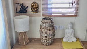 A wooden table with a lamp, a woven vase, a Buddha statue, and a shelf with decorative items.
