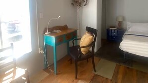 Ein Schlafzimmer mit einem Bett, einem Schreibtisch, einem Sessel, einem Nachttisch und einer Zimmerpflanze.