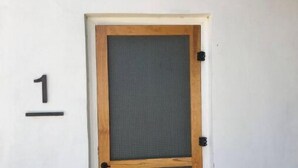 Eine Holztür mit Fensterglas, ein Schild mit der Nummer 1 an der Wand und eine Leuchte darüber.