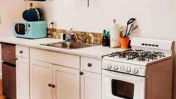 Una cocina con armarios blancos, estufa, microondas y pileta.