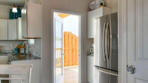 Une cuisine moderne avec des armoires blanches, un réfrigérateur en acier inoxydable et une terrasse en bois visible à travers une porte ouverte.