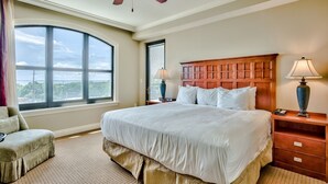 A hotel room with a large bed, a wooden headboard, a ceiling fan, a window with a view, a lamp, and a nightstand. - 3BR Destin condo Emerald Grande Harborwalk (Destin)