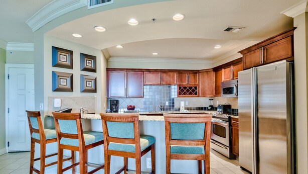 A modern kitchen with wooden bar stools, stainless steel appliances, and a large island. - 3BR Destin condo Emerald Grande Harborwalk (Destin)