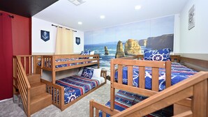 Een kamer met stapelbedden, een houten trap en een muurschildering van een kustlandschap.
