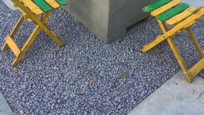 Un pozo de fuego cuadrado de hormigón con fuego encendido, rodeado por cuatro sillas de madera con cojines verdes.