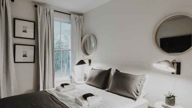 A neatly arranged bedroom with a bed, bedside table, lamp, and a small potted plant. - Classy Mid-Century Victorian ★ Ground-Floor ★ 2 Blocks from Forsyth Park (Savannah)