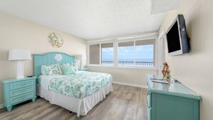 A bedroom with a bed, a nightstand, a dresser, a TV, and a window with a view.