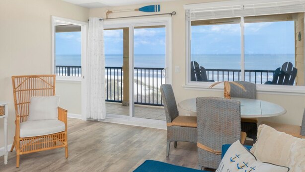 A room with a view of the beach, a ceiling fan, a wicker chair, a round table, and a sofa.