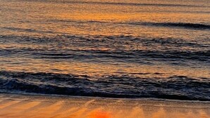 A sunset over a calm sea with gentle waves, reflecting the sky's orange hues.