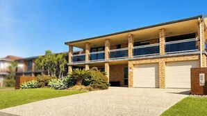 A two-story house with a covered balcony, a garage, and a well-maintained lawn. - Sea Sounds - Ultimate beachhouse with views (Caves Beach)
