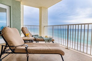 A balcony with two lounge chairs, a small table, and a view of the ocean.