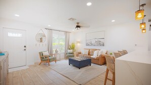 Ein geräumiges Wohnzimmer mit Holzboden, einem blauen Pouf, einem beigen Sofa und einem Essbereich mit einem Marmortisch.