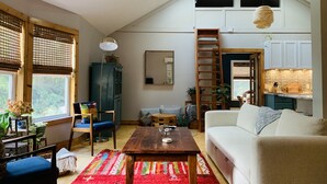 Ein gemütliches Wohnzimmer mit hohen Decken, einer Holzleiter, einem Esstisch und einem Sofa.