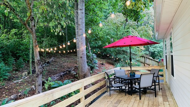 Eine Holzterrasse mit Tisch und Stühlen, umgeben von einem Holzzaun und Lichterketten.