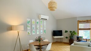 Ein modernes Wohnzimmer mit Essbereich, einem Flachbildfernseher und einem großen Fenster mit Jalousien.