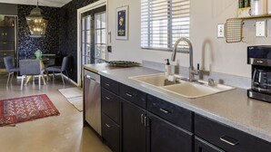 A modern kitchen with dark cabinetry, a large island, and a coffee machine. - Chasing The Moon: Walk to Pappy's & Tub Views (Pioneertown)