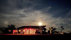 A building with a covered porch and a small attached structure, possibly a garage or shed, under a starry sky with a visible moon. - Chasing The Moon: Walk to Pappy's & Tub Views (Pioneertown)