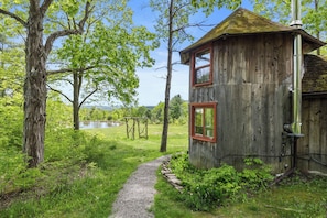 Un rustico chalet in legno con un vialetto sterrato che vi conduce, immerso nel verde e affacciato su un lago.