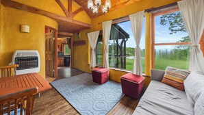 Une pièce chaleureuse avec un plafond en bois, une grande fenêtre avec des rideaux, un canapé, une table et un radiateur.