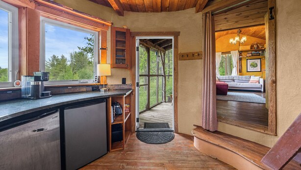 Un intérieur en bois comprenant une cuisine, un coin repas et une vue sur l’extérieur, visible à travers une porte.