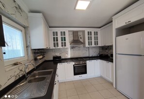 A kitchen with white cabinets, a black countertop, a sink, a stove, and a refrigerator. - family friendly villa with private garden and pool (Muğla)