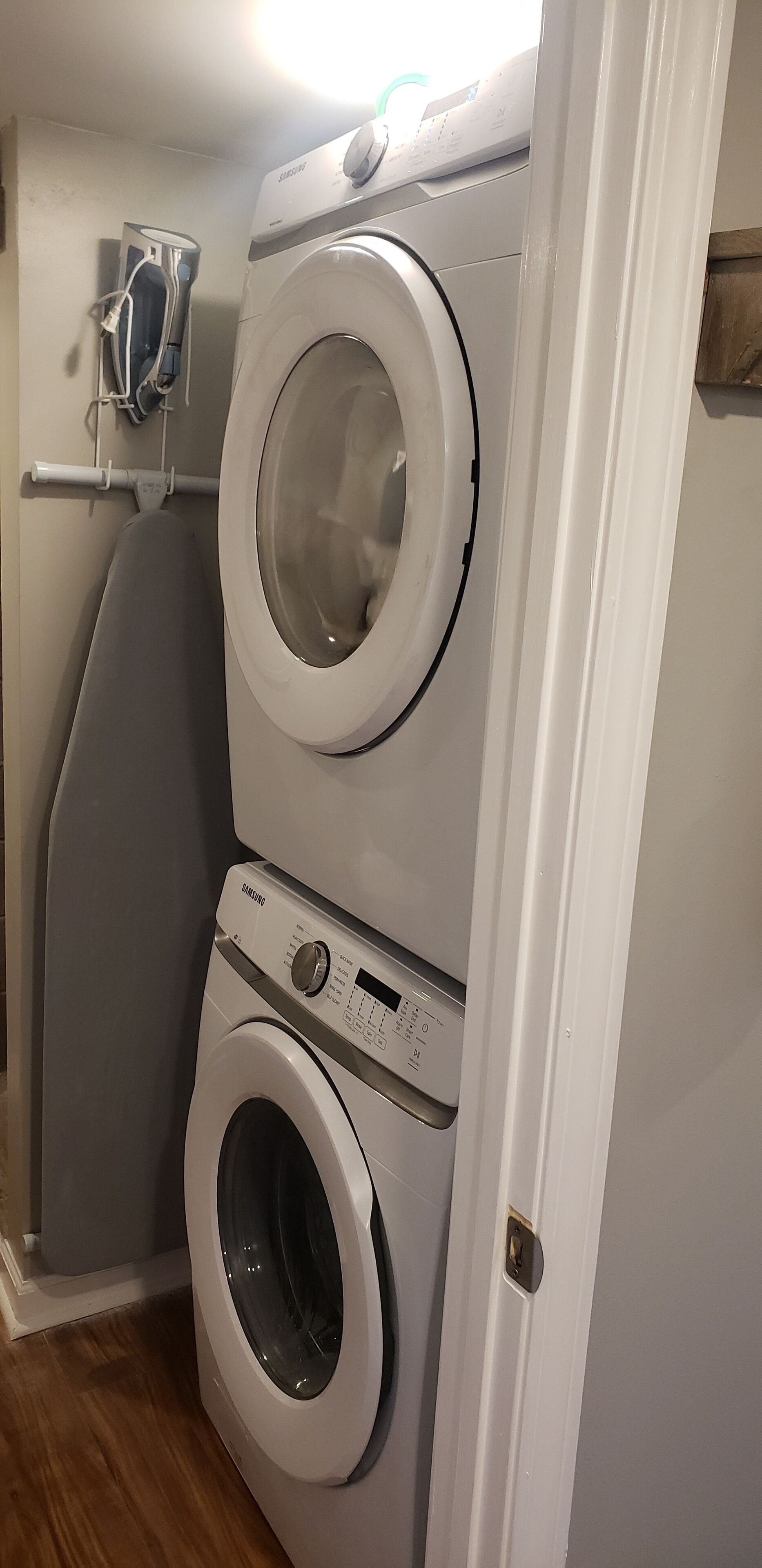A stacked washer and dryer unit in a laundry room with a wooden floor and a white door.