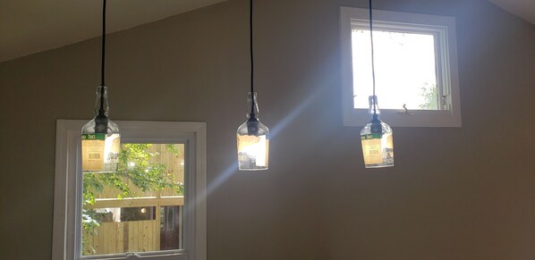 Three pendant lights hanging from the ceiling, a window with a view of a wooden deck and greenery, and a door with a sign on it.