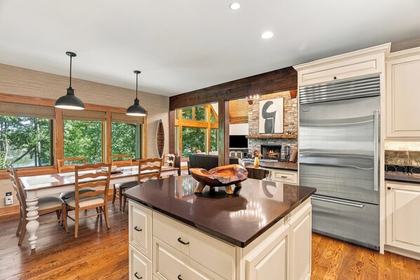 A modern kitchen with a large island, stainless steel appliances, and a dining area with wooden furniture.