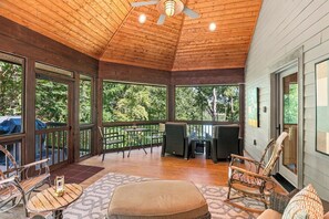 A covered outdoor area with a ceiling fan, wooden flooring, and a seating arrangement including chairs and a table.