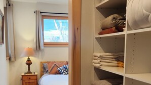 A bedroom with a bed, a nightstand, a lamp, a closet with shelves of folded towels, and a view of the outside through a window. - Clean, one bedroom, newly constructed home within walking distance of downtown.  (Bozeman)