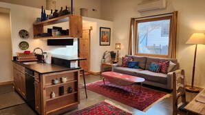 A compact living space with a kitchenette, a sofa, a coffee table, and a large window. - Clean, one bedroom, newly constructed home within walking distance of downtown.  (Bozeman)