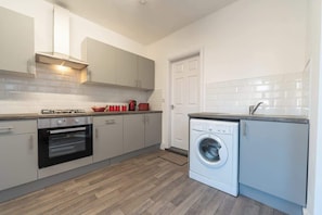 A modern kitchen with grey cabinets, a built-in oven, a washing machine, and a white tiled backsplash. - WGcDDE Large 3 Bedroom House - Parking - Garden (Kingston upon Hull)