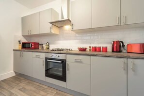 A modern kitchen with white cabinets, a built-in oven, a microwave, and red appliances. - WGcDDE Large 3 Bedroom House - Parking - Garden (Kingston upon Hull)