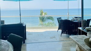 A balcony with two blue umbrellas, a dining table, chairs, and a view of the sea.