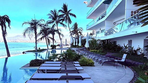 A poolside area with lounge chairs, palm trees, and a view of the ocean.