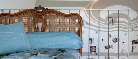 Un dormitorio con cabecera de madera, colcha estampada con motivos florales y una pared decorada con fotografías.