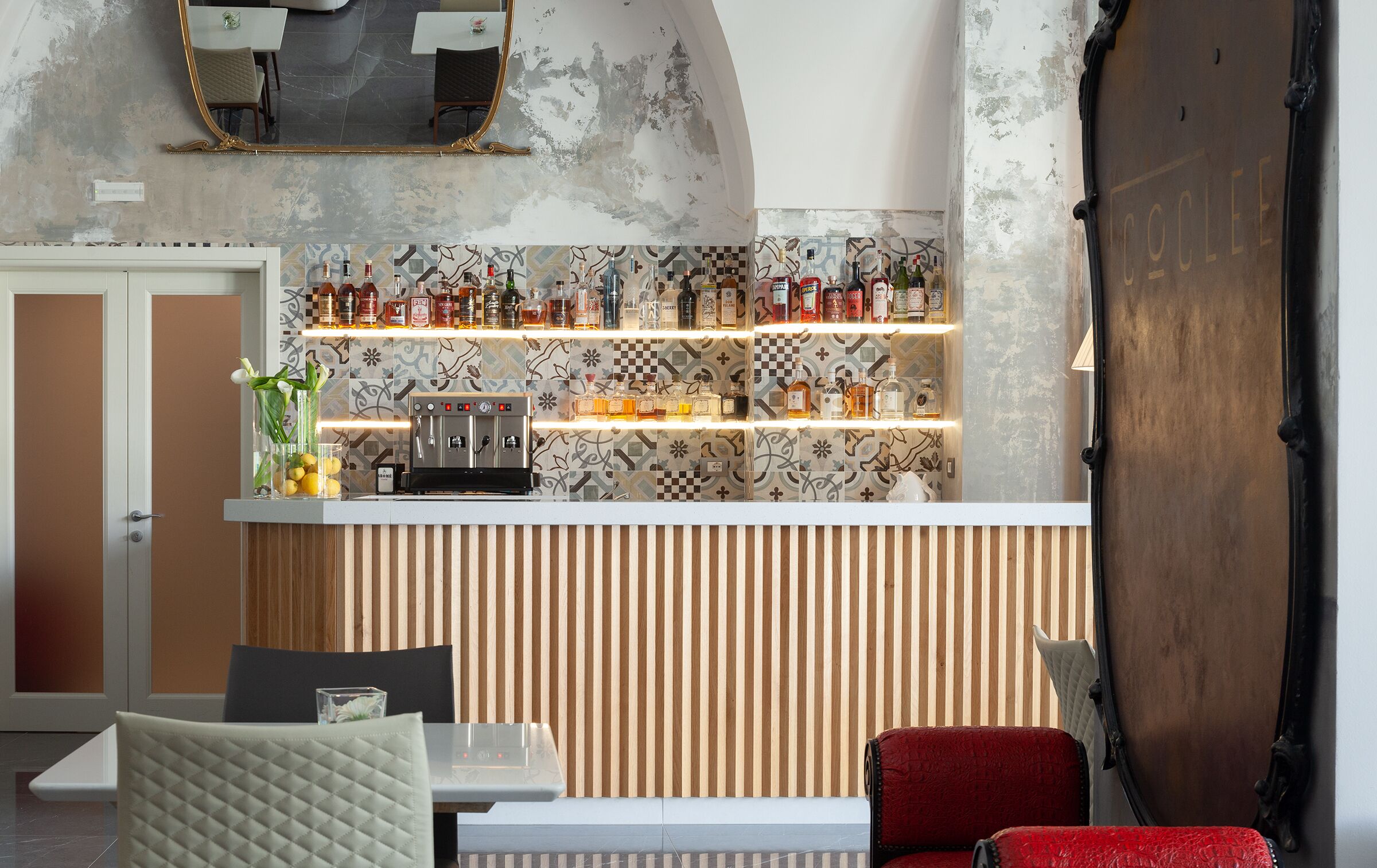 A bar area with a coffee machine, shelves of bottles, and a mirror above.