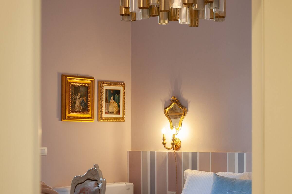 Un dormitorio con una cama, una silla, una mesita de noche y una lámpara fijada a la pared.
