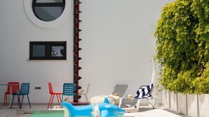 Zona de piscina con juguetes de tiburón inflables, sillas de descanso y seto.