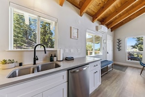 A modern kitchen with a large window, wooden ceiling beams, and a view of trees. - Tahoe Mountain Condo with Tree Filtered Lake Views. (Stateline)