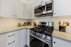 A modern kitchen with white cabinetry, a stainless steel range, a microwave, and a coffee maker. - Tahoe Mountain Condo with Tree Filtered Lake Views. (Stateline)