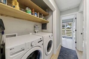 A laundry room with two LG washing machines, a shelf with cleaning products, and a view through an open door.
