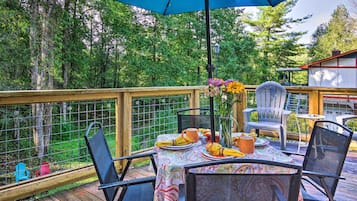 A wooden deck with a table set for dining, surrounded by chairs, and an umbrella providing shade.