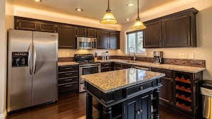 A modern kitchen with dark wood cabinets, stainless steel appliances, granite countertops, and pendant lighting. - Hot Tub | Theater | Firepit | Gym | Yard | Foosbal (Colorado Springs)