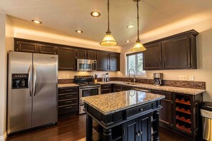 Una cocina moderna con alacenas de madera oscura, electrodomésticos de acero inoxidable, encimeras de granito e iluminación colgante.