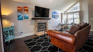 A living room with a fireplace, a sofa, a TV, and artwork on the walls. - Hot Tub | Theater | Firepit | Gym | Yard | Foosbal (Colorado Springs)