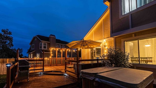 A wooden deck with a hot tub, outdoor seating, and string lights. - Hot Tub | Theater | Firepit | Gym | Yard | Foosbal (Colorado Springs)